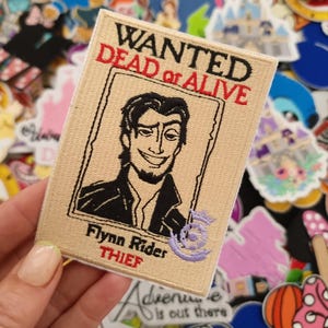 May include: A tan patch with the text "WANTED DEAD or ALIVE" in black and red. It features a black and white portrait of Flynn Rider and the word "THIEF". A purple embroidered number 5 is on the right side.