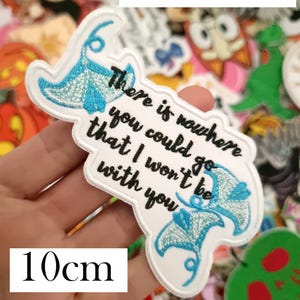 K&ouml;nnte beinhalten: Ein wei&szlig;er, gestickter Aufn&auml;her mit dem Zitat "There is nowhere you could go that I won't be with you" und zwei blauen Mantarochen-Designs. Der Aufn&auml;her ist 10 cm lang und tr&auml;gt oben die Worte "Moana Quote".