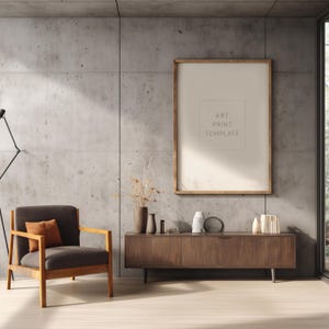 Puede incluir: Una escena interior moderna con una plantilla de impresión artística enmarcada en madera sobre una pared de hormigón. Un sillón gris oscuro con brazos de madera y un cojín naranja se encuentra en un suelo de madera clara. Un mueble de madera con objetos decorativos debajo.