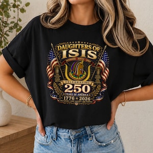 Peut inclure: T-shirt noir avec un motif graphique comportant le texte "DAUGHTERS OF ISIS" et "CELEBRATING 250 YEARS OF AMERICA 1776-2026". Le motif comprend des drapeaux américains, des colonnes et une tête de style égyptien.
