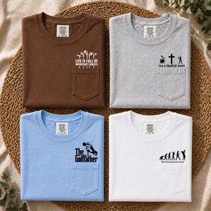 May include: Four t-shirts in brown, gray, light blue, and white, each with a pocket and a golf-themed graphic. The brown shirt says "Life is full of important choices." The gray shirt says "I'm a simple man." The light blue shirt says "The Golffather." The white shirt says "The Evolution of Man."
