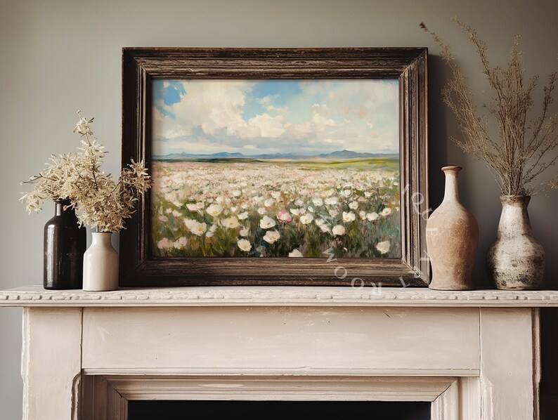 May include: A framed painting of a field of white flowers with a blue sky and white clouds in the background. The painting is hanging on a white mantelpiece above a fireplace.