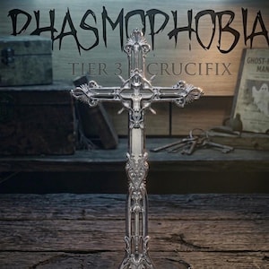 Peut inclure: Croix argentée ornée avec des détails complexes, représentant une figure centrale. Le texte "Phasmophobia Tier 3 Crucifix" est visible dans une police gothique, sur un fond en bois rustique avec d'autres accessoires.