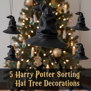 Könnte beinhalten: Fünf schwarze Weihnachtsbaumschmuck-Sortierhüte hängen vor einem Weihnachtsbaum mit Lichtern und Ornamenten. Die Hüte sind Nachbildungen aus der Harry-Potter-Reihe. Das Bild zeigt auch Geschenkboxen.