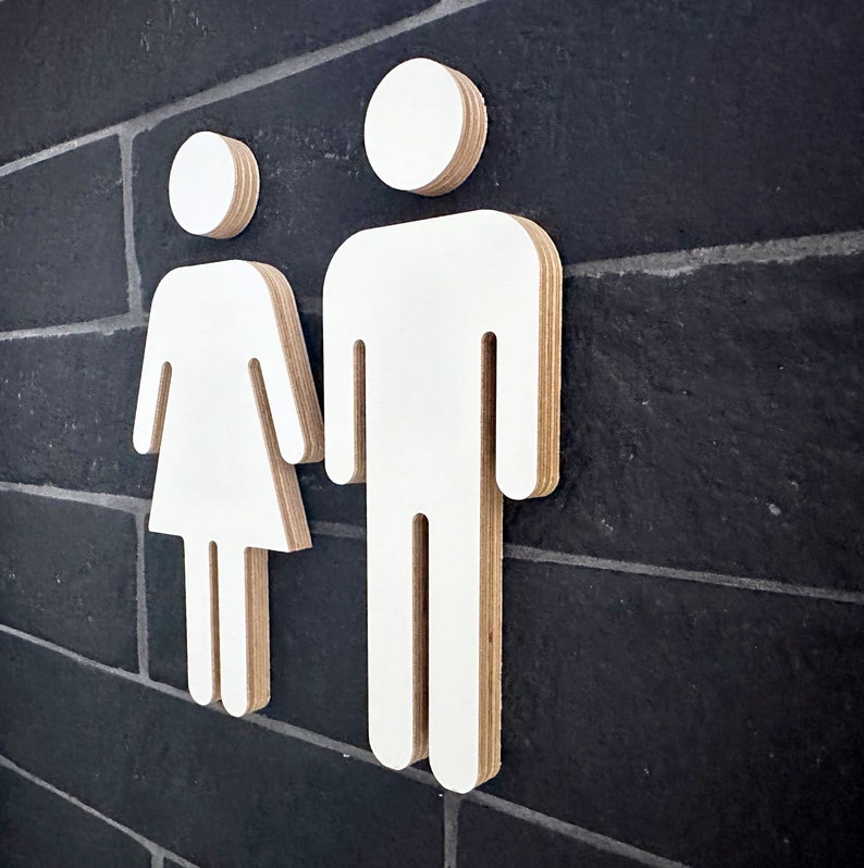 May include: White wooden cutout of a male and female figure, representing a restroom sign.