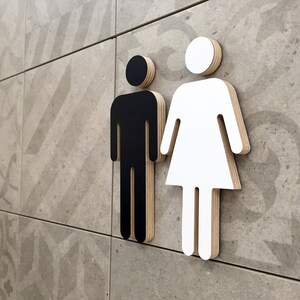 May include: Black and white gender symbol signs on a tiled wall. The male symbol is black and the female symbol is white.