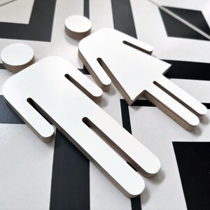 May include: Two white wooden cutout figures, one with a skirt and the other with pants, are displayed on a black and white patterned surface.