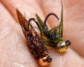 Può includere: Due esche da pesca a mosca con piume marroni e verdi e perline dorate.