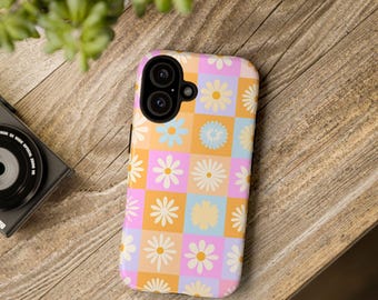Puede incluir: Una funda rectangular para smartphone con un patrón de tablero de ajedrez repetitivo de cuadrados de color rosa claro, naranja y azul claro. Cada cuadrado contiene un gráfico de margarita blanca con centro amarillo. La funda tiene un recorte negro.