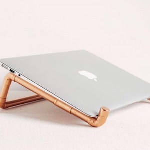 May include: A copper laptop stand made from pipes. The stand is angled to elevate a laptop for better ergonomics.