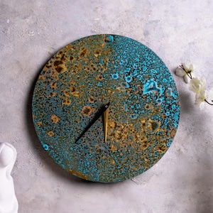 May include: A round clock with a blue and gold metallic finish. The clock face has a unique, speckled pattern and features black and gold hands.