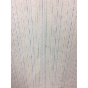 May include: A white fabric featuring a vertical pinstripe pattern in alternating light blue and pale yellow colors. The textile displays a subtle diagonal weave texture throughout the surface, with a small, faint brown spot visible near the center.
