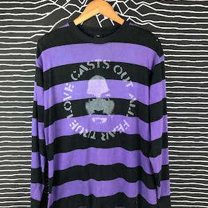 May include: Purple and black striped long-sleeve shirt with a graphic print of a face in a circle. The text around the face reads "Love Casts Out All Fear."