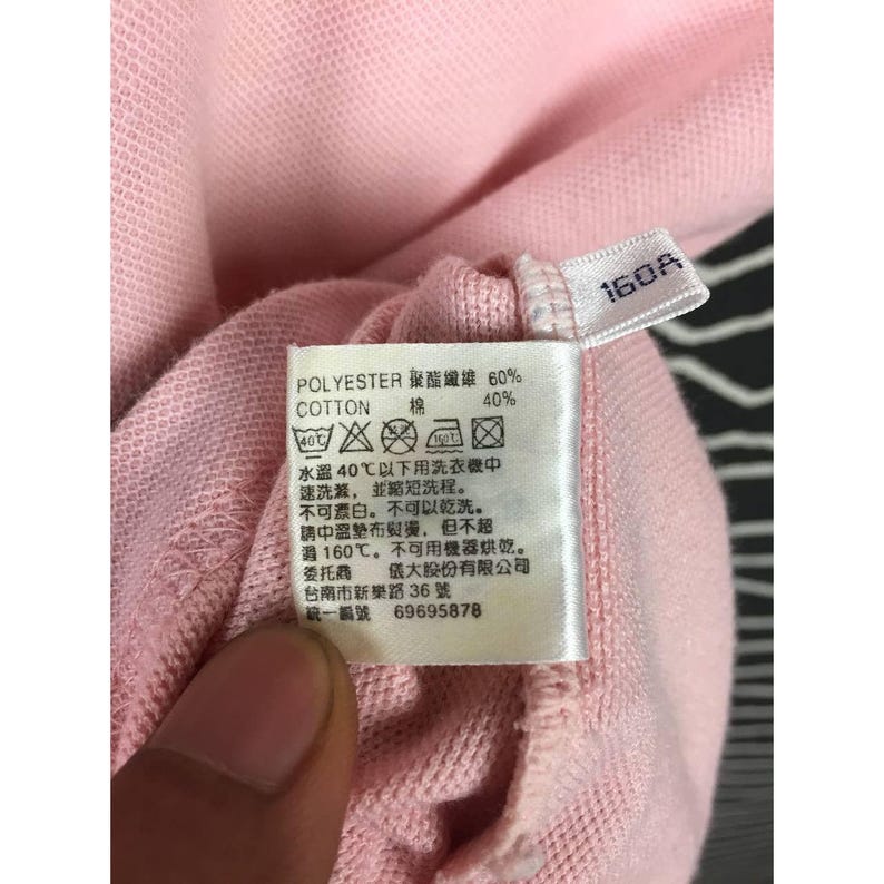 May include: Close-up of a pink garment tag with text in Chinese and English. The tag lists the fabric composition as 60% polyester and 40% cotton, along with care instructions. The tag also includes the number "160A".