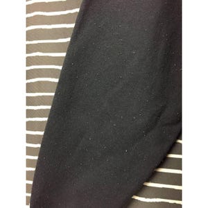May include: Close-up of a black fabric with a slightly textured surface. The fabric is covered in small, light-colored particles. The background features a striped pattern in shades of brown and white.