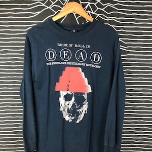Op de afbeelding: Een marineblauw longsleeve t-shirt met een schedelgraphic die een rode hoed draagt. De tekst "Rock 'n' Roll is DEAD" is in witte cirkels boven de schedel gedrukt. De tekst "The Freshjive Seditionary Movement" is onder de schedel gedrukt.