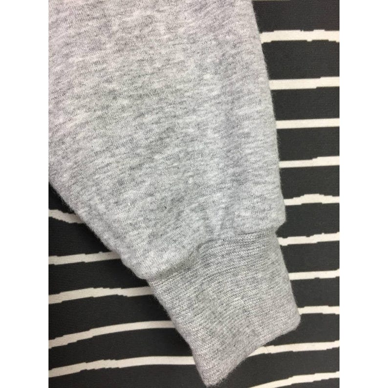 Peut inclure: Gros plan sur une manche de sweat-shirt grise. Le poignet est c&ocirc;tel&eacute; et le tissu a une texture chin&eacute;e. Le fond est un motif &agrave; rayures noires et blanches.