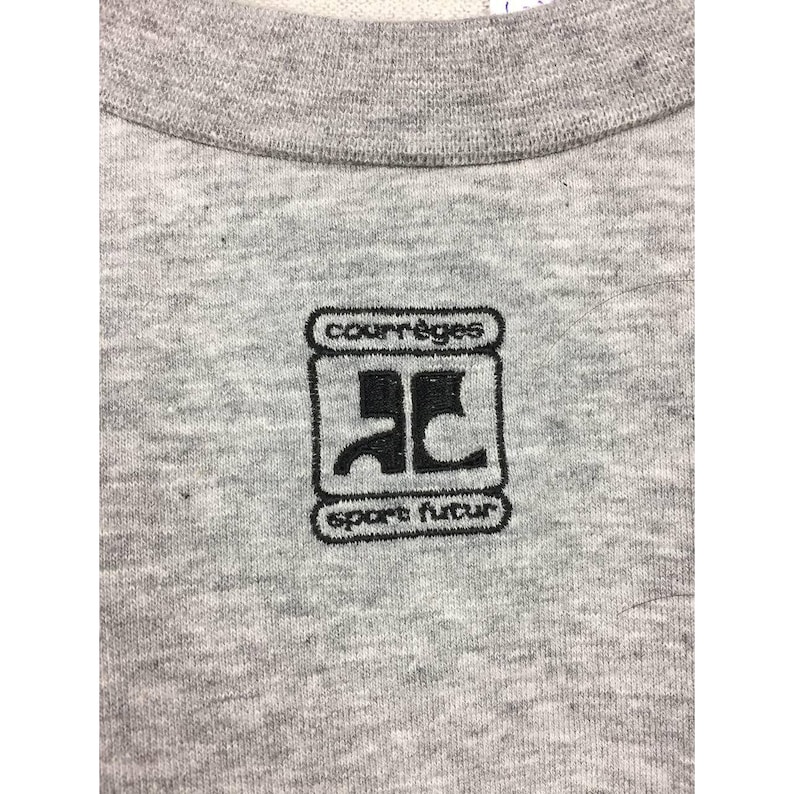 Peut inclure: Gros plan sur un sweat-shirt gris chin&eacute; avec un logo brod&eacute; noir. Le logo comprend le nom de la marque "courr&egrave;ges" au-dessus d'un design stylis&eacute; et les mots "sport futur" en dessous.