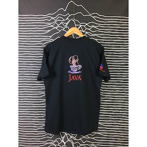 May include: Black t-shirt with a graphic of a coffee cup and the word "JAVA" in red. The design is on the back of the shirt. The shirt is hanging on a wooden hanger against a black and white striped background.