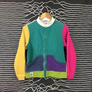 Peut inclure: Un cardigan multicolore avec une fermeture à boutons pression. Le cardigan est fait d'un mélange de coton doux et présente une variété de couleurs, notamment le jaune, le vert, le bleu, le violet et le rose.