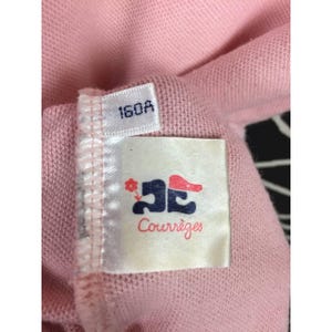 May include: Close-up of a pink fabric with a tag. The tag has the number "160A" printed on it. Below the number is a white tag with a logo and the word "Courr&egrave;ges" in red script.