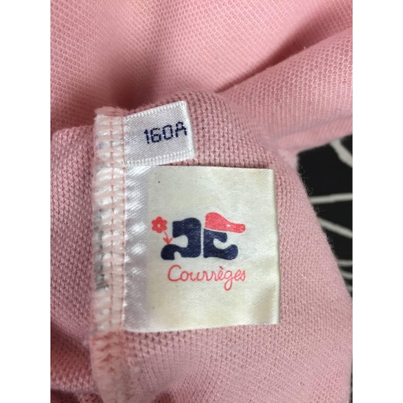 May include: Close-up of a pink fabric with a tag. The tag has the number "160A" printed on it. Below the number is a white tag with a logo and the word "Courr&egrave;ges" in red script.