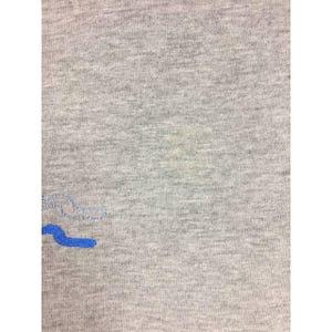 Peut inclure: Gros plan d'un t-shirt gris avec un motif brod&eacute; bleu. Le tissu a un aspect textur&eacute;. Le motif bleu est une forme stylis&eacute;e.