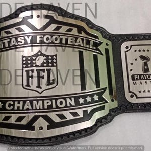 Puede incluir: Un cinturón negro y plateado de campeón de fútbol de fantasía. El cinturón presenta una placa central grande con el texto "FANTASY FOOTBALL CHAMPION" y las letras "FFL". Dos placas laterales dicen "PLAYOFFS MASTER".