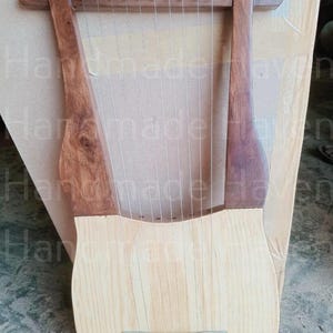 May include: A wooden lyre with 10 strings, a light brown body, and dark brown arms. The lyre is handmade and has a natural wood finish.