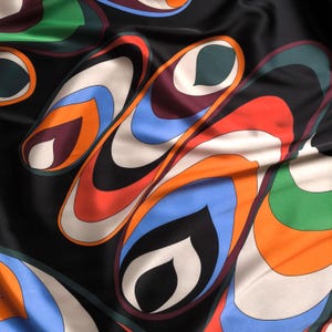 May include: Black fabric with a vibrant, abstract pattern. The design features layered, elongated shapes in shades of orange, blue, white, green, and burgundy, set against a black background. The fabric has a glossy sheen.