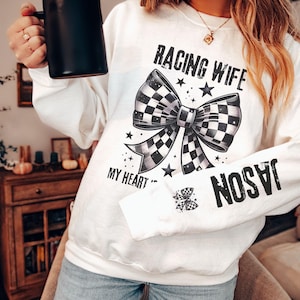 May include: White sweatshirt with the text "RACING WIFE" above a checkered bow graphic. The sleeve features the name "JASON" in bold black letters. The words "MY HEART" are below the bow.