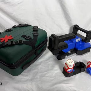 Op de afbeelding: Een donkergroene EHBO-kit met een rood kruis embleem, zwarte bandjes en gespen. Een blauw en zwart apparaat, samen met twee witte en rode containers, zijn ook aanwezig. De afbeelding bevat de tekst "OddsEnds More".