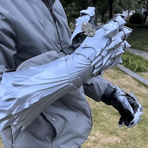 May include: Silver dragon-scale gauntlets with articulated segments and spiked accents. The gauntlets have detailed metallic clasps. The image also shows a grey jacket and jeans. The gauntlets are designed to look like dragon scales.
