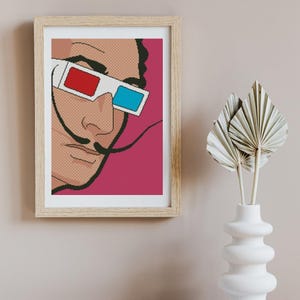 May include: A framed wall art print featuring a pixelated pop art illustration of a person with a prominent mustache wearing 3D glasses with red and blue lenses against a solid magenta background, enclosed in a light-colored wooden frame.
