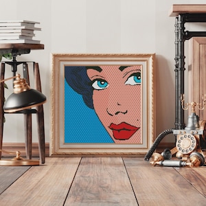 May include: A framed pop art print of a woman's face with blue eyes, red lips, and blue hair. The background is a blue and white pattern.