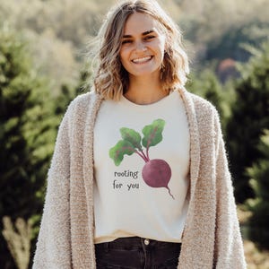 以下が含まれることがあります： ビーツのグラフィックと「rooting for you」というテキストが書かれた白いTシャツです。