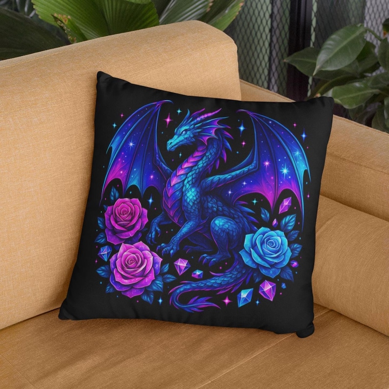 May include: A square throw pillow featuring a black background with a central illustration of a blue and purple dragon with large wings. The dragon is surrounded by vibrant pink and blue roses, scattered geometric crystals, and small glowing stars.