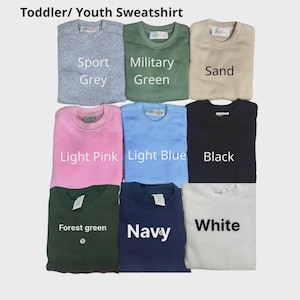 May include: A collection of nine toddler and youth crewneck sweatshirts in various colors including sport grey, military green, sand, light pink, light blue, black, forest green, navy, and white, with the text Toddler/ Youth Sweatshirt at the top.