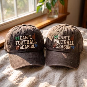 Op de afbeelding: Twee donkerbruine baseballpetten met de geborduurde tekst CAN'T. FOOTBALL SEASON. Het ontwerp bevat een groene strik, een bruine schuimvinger, een bruine football en een blauwe strik, allemaal geborduurd op de voorkant van de katoenen petten.