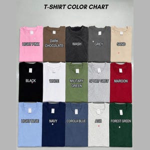 May include: A T-shirt color chart displaying fifteen folded crew neck shirts in various colors including light pink, dark chocolate, wash, grey, sand, black, white, military green, sport grey, maroon, light blue, navy, corola blue, ash, and forest green.