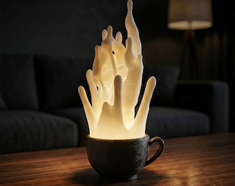 May include: A decorative lamp featuring a dark brown coffee cup with a textured design, holding a white, illuminated splash. The light creates a warm ambiance. The lamp sits on a wooden table, with a dark background.