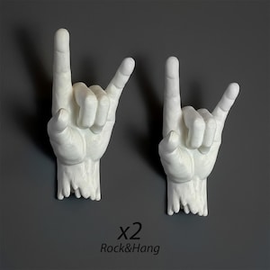 Puede incluir: Dos esculturas de manos blancas en el gesto de 'rock on', montadas sobre un fondo gris. El texto "x2 Rock&Hang" está debajo. Las manos están detalladas con nudillos visibles y superficies texturizadas.