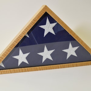 May include: A wooden triangular frame with a glass front displays a folded American flag. The flag is navy blue with white stars.