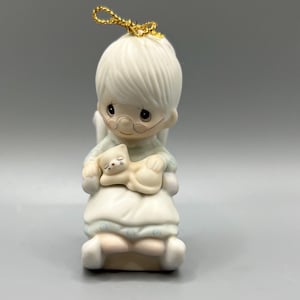 Puede incluir: Una figurita de porcelana blanca de una abuela sosteniendo un gato blanco. La figurita lleva un vestido azul y blanco y gafas. La figurita está sentada en una mecedora.