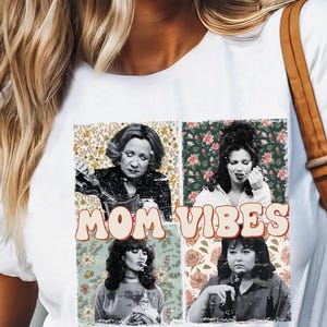 Pu&ograve; includere: Maglietta bianca con una grafica in stile vintage che presenta quattro donne con sfondi floreali e il testo "MOM VIBES".