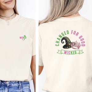 May include: A white t-shirt with a green and pink graphic on the back that says "Changed for Good" with a witch's hat and a crown. The front of the shirt has a small green and pink graphic that says "Wicked".