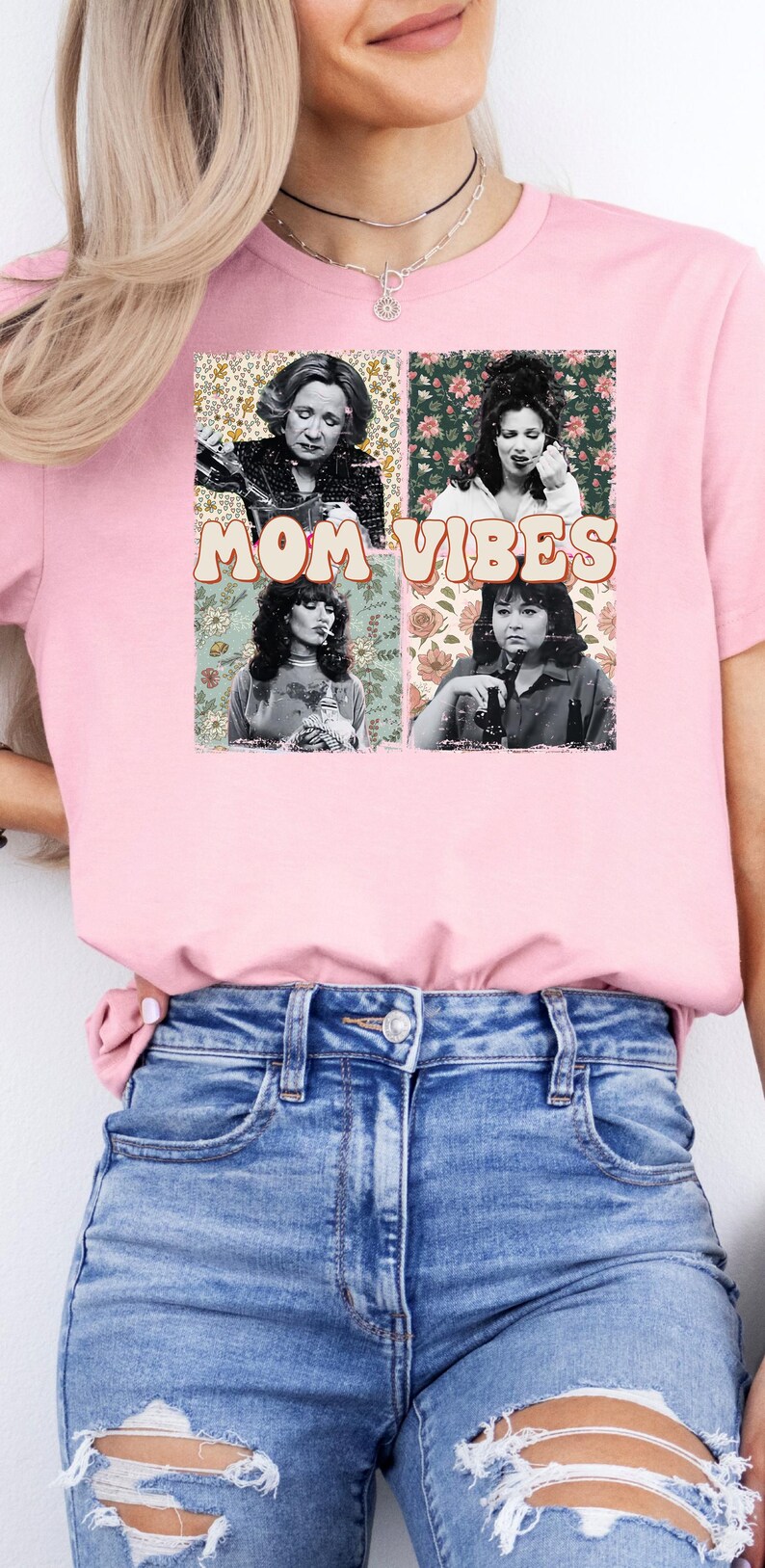 Pu&ograve; includere: Maglietta rosa con un collage di quattro volti di donne e motivi floreali. Il testo "MOM VIBES" &egrave; stampato in un font retr&ograve;.