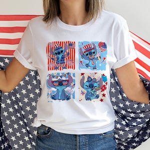 May include: White t-shirt with a four-panel design of a blue cartoon character in patriotic attire. The character is shown with sunglasses, a hat, and holding a balloon, all in red, white, and blue. The background includes fireworks and flags.