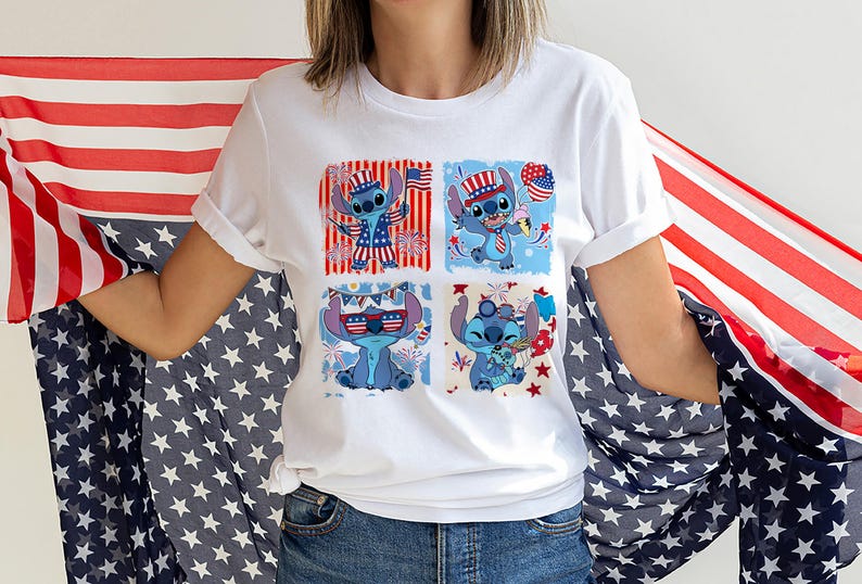 May include: White t-shirt with a four-panel design of a blue cartoon character in patriotic attire. The character is shown with sunglasses, a hat, and holding a balloon, all in red, white, and blue. The background includes fireworks and flags.