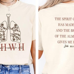 May include: A beige t-shirt with a brown outline of lungs with floral details. The text "YHWH it's your breath for your lungs" is printed below the lungs. The back of the shirt has the text "THE SPIRIT OF GOD HAS MADE ME, AND THE BREATH OF THE ALMIGHTY GIVES ME LIFE. Job 33:4" printed in brown.